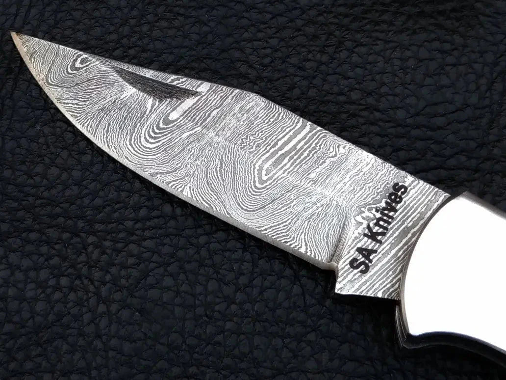 Damascus steel folding knife on black leather surface